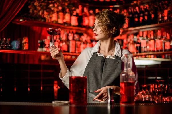 Mooie vrouw barman aan bar en houdt glas cocktail en kijkt ernaar — Stockfoto