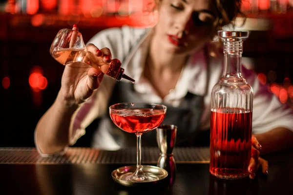 Close-up of glass with drink to which woman bartender adds ingredient from small bottle — Stock Photo, Image