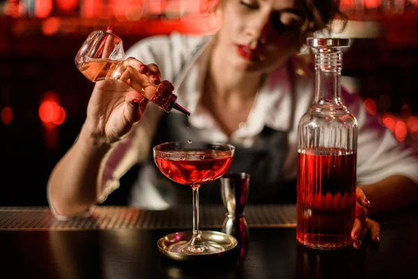 View of glass with drink to which woman bartender adds ingredient from small bottle — Stock Photo, Image