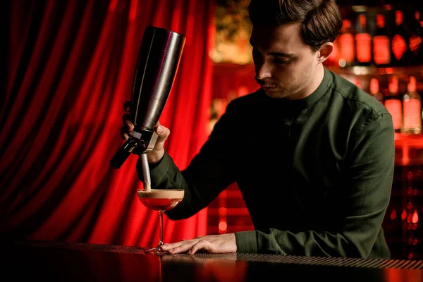 Mann an Bar hält Werkzeug in der Hand und fügt Glas mit alkoholischem Cocktail Schaum hinzu — Stockfoto