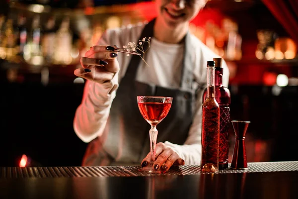 Bela vista de vidro com bebida alcoólica brilhante que bartender mulher decora com ramo florido — Fotografia de Stock