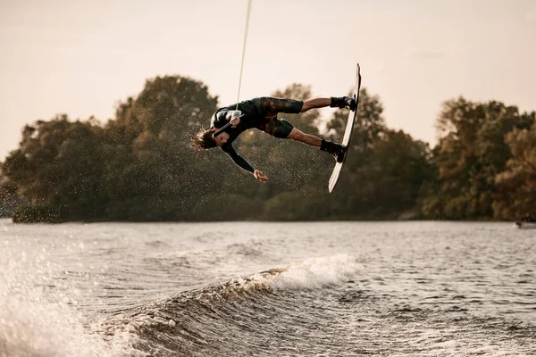 Homme musclé énergique tient la corde et fait magistralement flips avec wakeboard sur éclaboussures d'eau — Photo