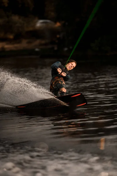 Pemuda yang aktif dalam pakaian basah naik wakeboard cepat pada percikan air sungai — Stok Foto