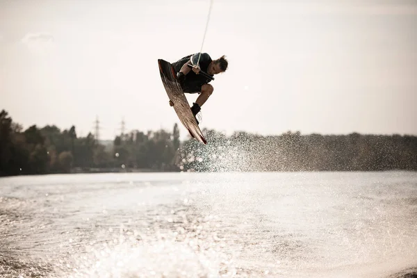 Schöne Aussicht auf jungen sportlichen Mann, der hoch oben auf dem Wakeboard über dem Wasser springt — Stockfoto