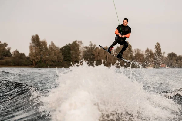 Mannelijke wakeboarder houdt de kabel vast en springt op spetterende golf van rivier. — Stockfoto