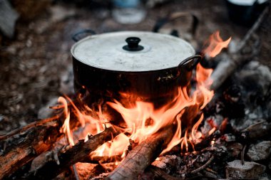 Demir tencereye yakın çekim. Kapağı yanan odunun üzerinde duruyor..