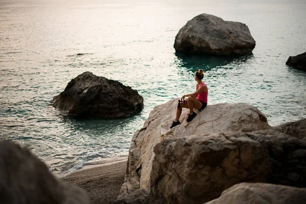 Utsikt över kvinnan sitter på enorm sten på stranden och tittar bort — Stockfoto