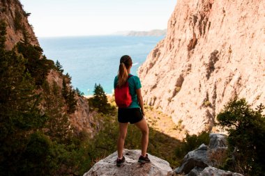Sırt çantalı kadının dikiz aynası taşın üzerinde duruyor ve dağ manzarasının keyfini çıkarıyor..