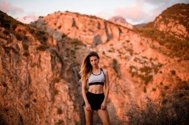 Güzel bir kadın, gün ışığıyla aydınlatılmış dağın arka planında duruyor.