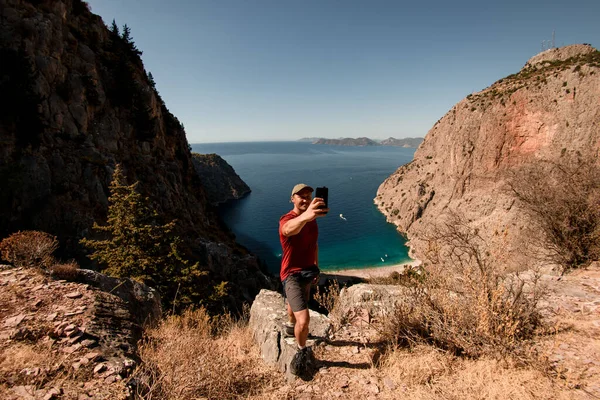 Leende man tar selfie på toppen av berget mot havet landskap. — Stockfoto