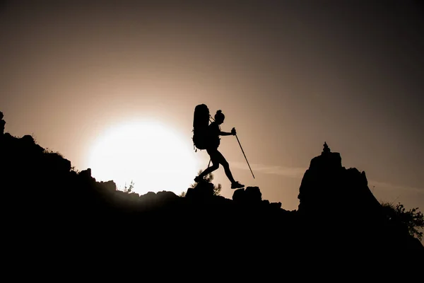awesome view of female silhouette with tourist equipment walking along rocky path against sun