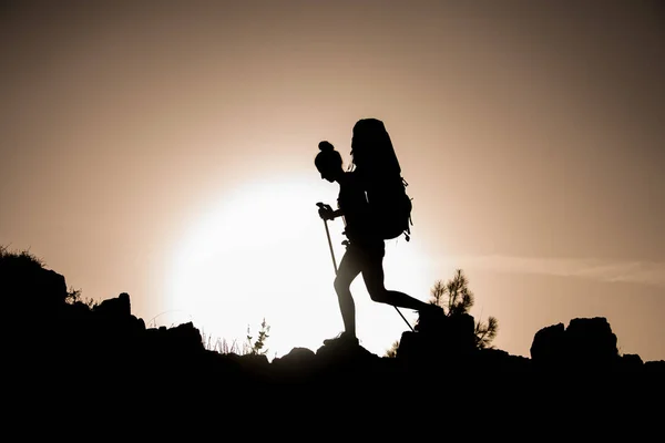 Silhuett av kvinna turist med trekking pinnar och ryggsäck som går mot solen — Stockfoto