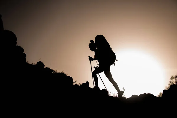 Silhuett av kvinna turist med trekking pinnar och ryggsäck som går längs stenig väg — Stockfoto