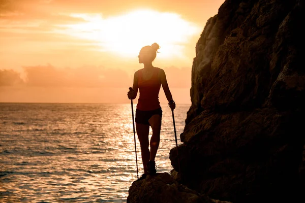beautiful view of female silhouette with trekking sticks near cliff on background with sunrise