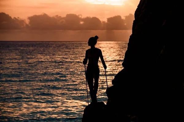 Fantastisk utsikt över kvinnliga silhuett med trekking pinnar nära klippan på bakgrunden med soluppgång — Stockfoto