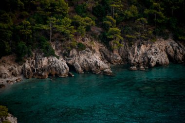 Yeşil çam ağaçları ve turkuaz renkli suyu olan kayalık bir uçurum..