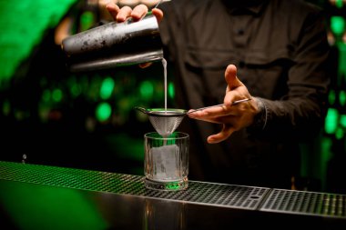 Erkek barmen karıştırıcıdan eski moda bardağa kokteyl döker.