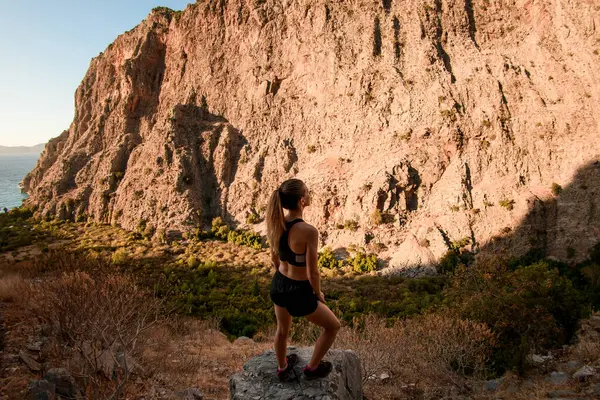 Taşın üzerinde duran ve dağ manzarasının keyfini çıkaran kadının yüksek açılı görüntüsü.