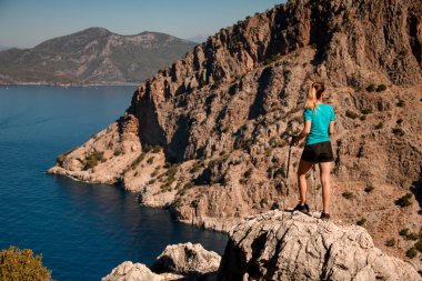 Büyük bir kayanın üzerinde duran ve deniz koyunun keyfini çıkaran kadının dikiz görüntüsü