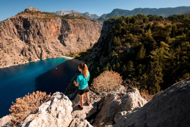 Büyük taşın üzerinde duran ve deniz koyunun keyfini çıkaran kadının yüksek açılı görüntüsü.