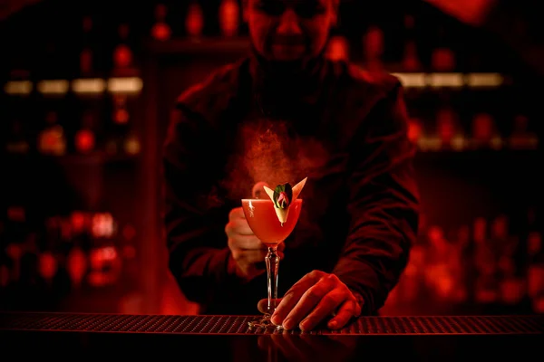 man bartender holds with his hand glass with cocktail on bar counter.