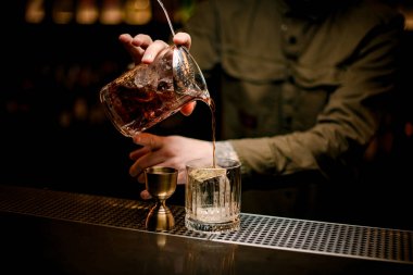 Bir barmenin eli bardağı soğuk kokteyl ile karıştırır ve eski moda bardağa doldurur.