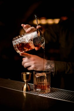 Barmenlerin el ele tutuşup bardağa kokteyl doldurdukları yakın plan.