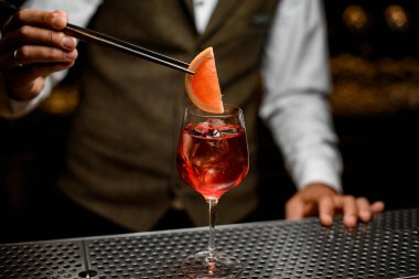 Barmen elinde portakal dilimli cımbızla buzlu kokteyl bardağı tutuyor.