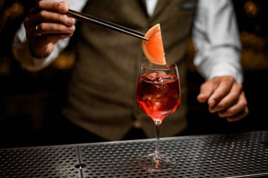 Barmen elinde portakal dilimli cımbızla buzlu kokteyl bardağı tutuyor.