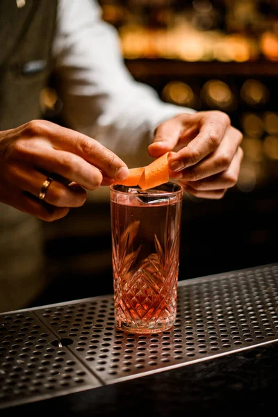 Vista sobre vidrio de cristal con bebida fría que manos barmans decorar con cáscara de naranja — Foto de Stock