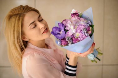 Çiçek buketi. Farklı mor çiçekler. Sarışın kadının ellerinde.