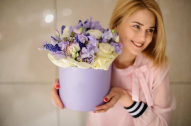 Leylak ve beyaz çiçeklerle dolu güzel yuvarlak kutu, neşeli bir kadının ellerinde.