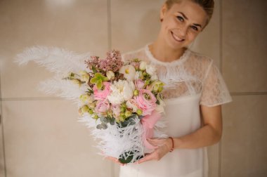 Kadının ellerinde beyaz tüylerle süslenmiş gül ve şakayık demetleri.