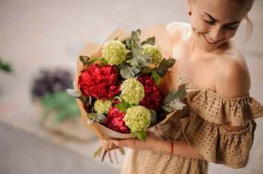 Kadının elinde kırmızı şakayıklardan oluşan muhteşem bir buket var.