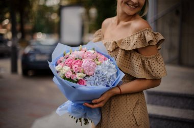 Gülümseyen bir kadının ellerinde bir buket renkli çiçek.