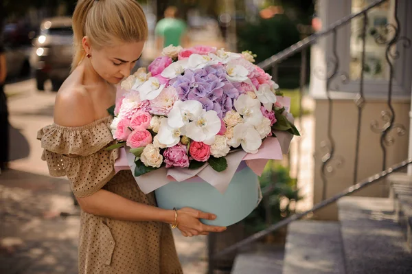 Jovem mulher loira detém caixa redonda com enorme buquê de flores diferentes e cheira — Fotografia de Stock
