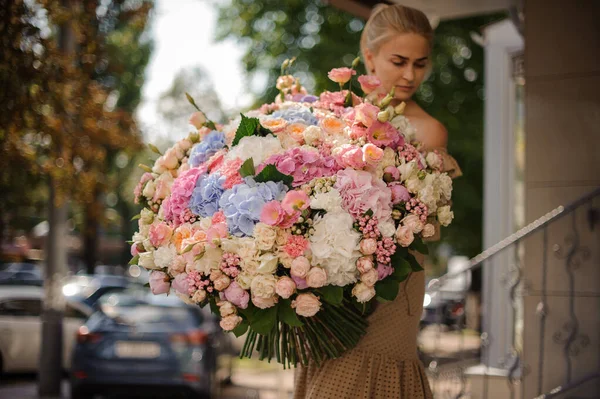 Incrível enorme monte de flores diferentes nas mãos de jovem mulher loira — Fotografia de Stock