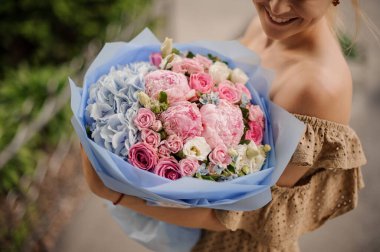 Gülümseyen bir kadının ellerinde kocaman bir buket renkli çiçek.