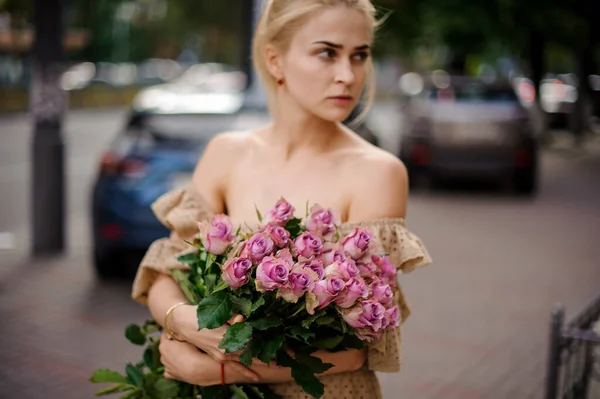 Junge blonde Frau hält sanft einen Strauß schöner lila Rosen in ihren Händen — Stockfoto