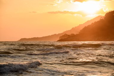 Deniz, dağlar ve akşam güneşli gökyüzü olan büyük bir dağ manzarası..
