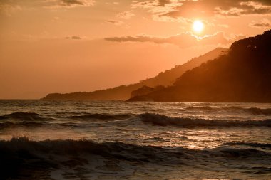 Deniz üzerinde büyüleyici bir gün batımı ve dağların manzarası. Güneşin yansıması, gökyüzü ve bulutlar.