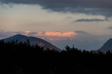 Gökyüzü bulutları üzerinde renkli ve canlı güneş ışığıyla dağ manzarası, doğa.