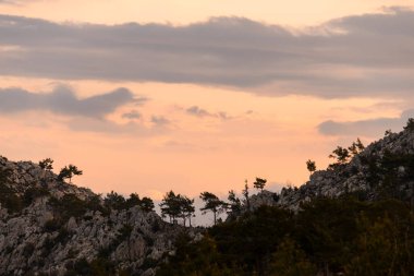 Parlak gündoğumu sırasında ağaçlı ve bulutlu kayalık dağ tepelerinin güzel manzarası..