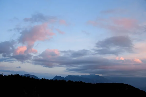 Céu bonito com nuvens vivas. Silhuetas escuras de montanhas e árvores ao amanhecer. — Fotografia de Stock
