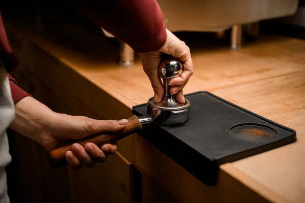 Female barista presses ground coffee using tamper. Close-up view on hands with portafilter — Stock Photo, Image