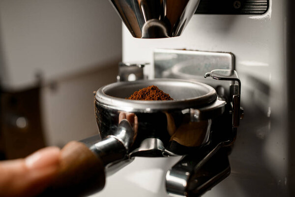 Close-up of portafilter full of ground coffee which pours from coffee grinder