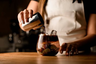 Kadınların elleri çelik bardakları tutar ve dikkatle kaseye soğuk bitkisel içeceklerle kahve koyar.