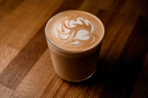 Bir bardak sıcak kahvenin manzarası ve ahşap masa arkasında güzel bir latte sanatı.. — Stok fotoğraf