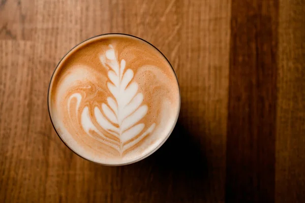 Ovanifrån av vackert vitt mönster på skummande latte i glas på träbord — Stockfoto