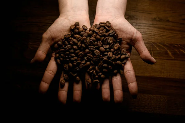 Vista superior de mãos femininas segurando grãos de café contra a superfície de madeira de fundo — Fotografia de Stock